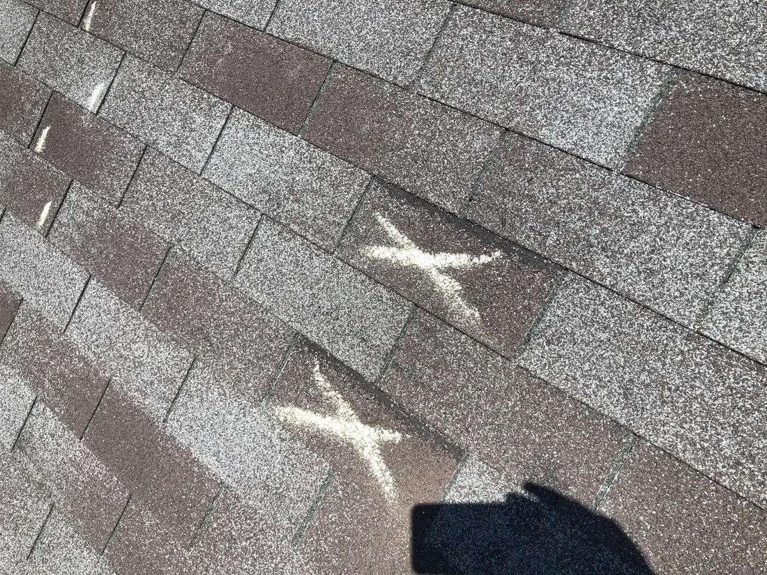 Storm-damaged asphalt shingles marked with chalk to document impact points for an insurance claim