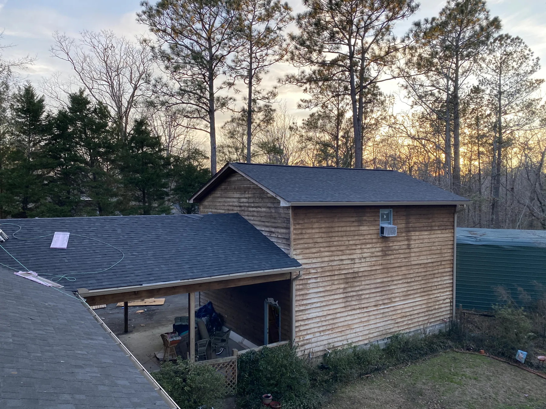 Patriots' Roofing finished shingle roof on a wood-sided home framed by tall pines in Eastern North Carolina
