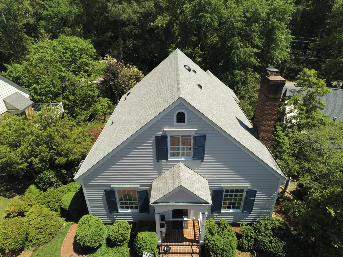 Aerial view of a finished gray shingle roof on a blue colonial home surrounded by trees in Eastern NC