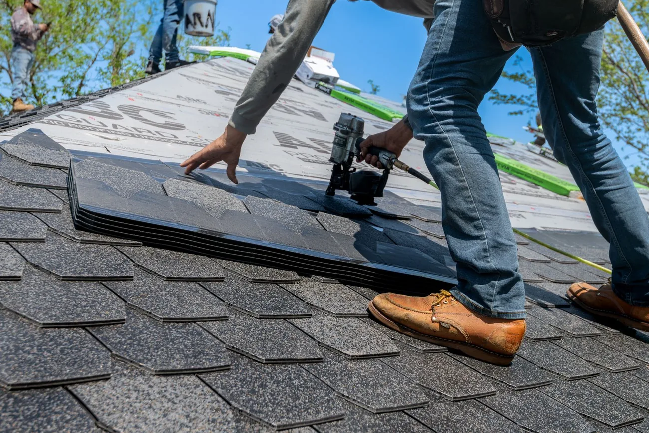 Roofer installing asphalt shingles with a nail gun during a roof repair